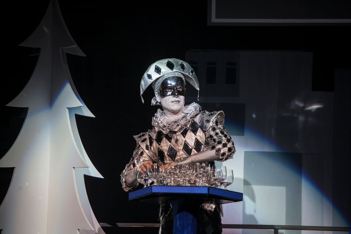 A man in a harlequin costume is standing at a podium