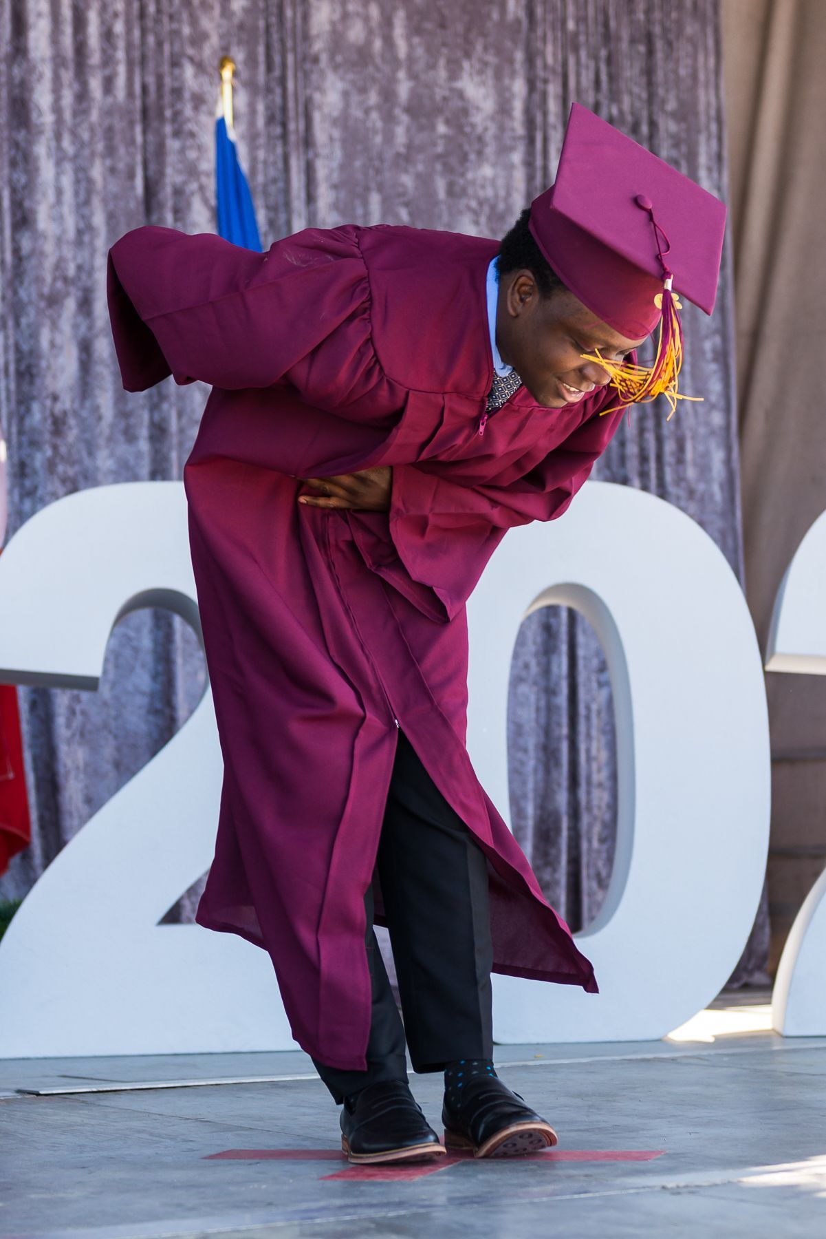 A man in a graduation cap and gown is kneeling down on a stage.