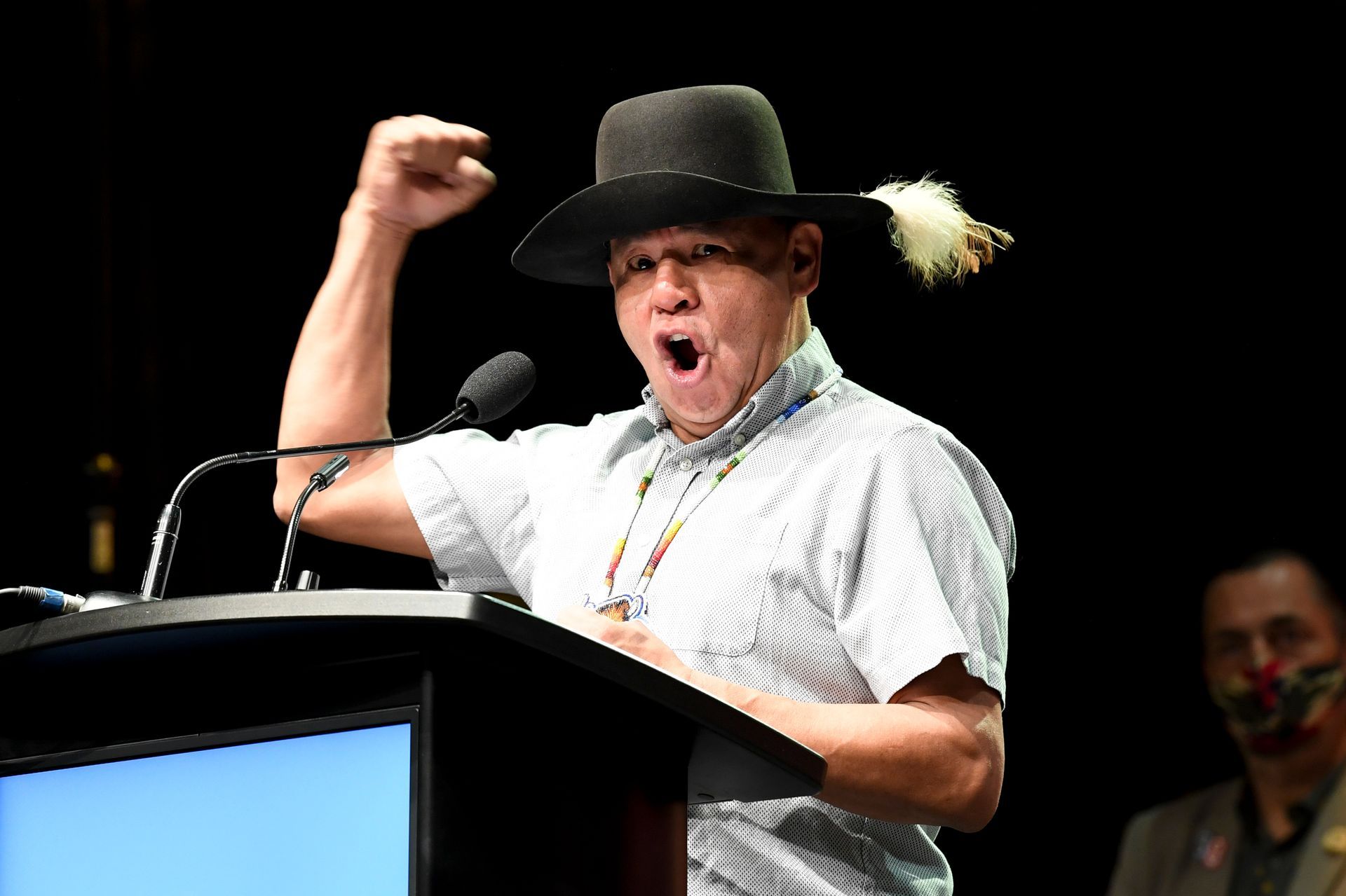 A man in a hat is standing at a podium with his fist in the air