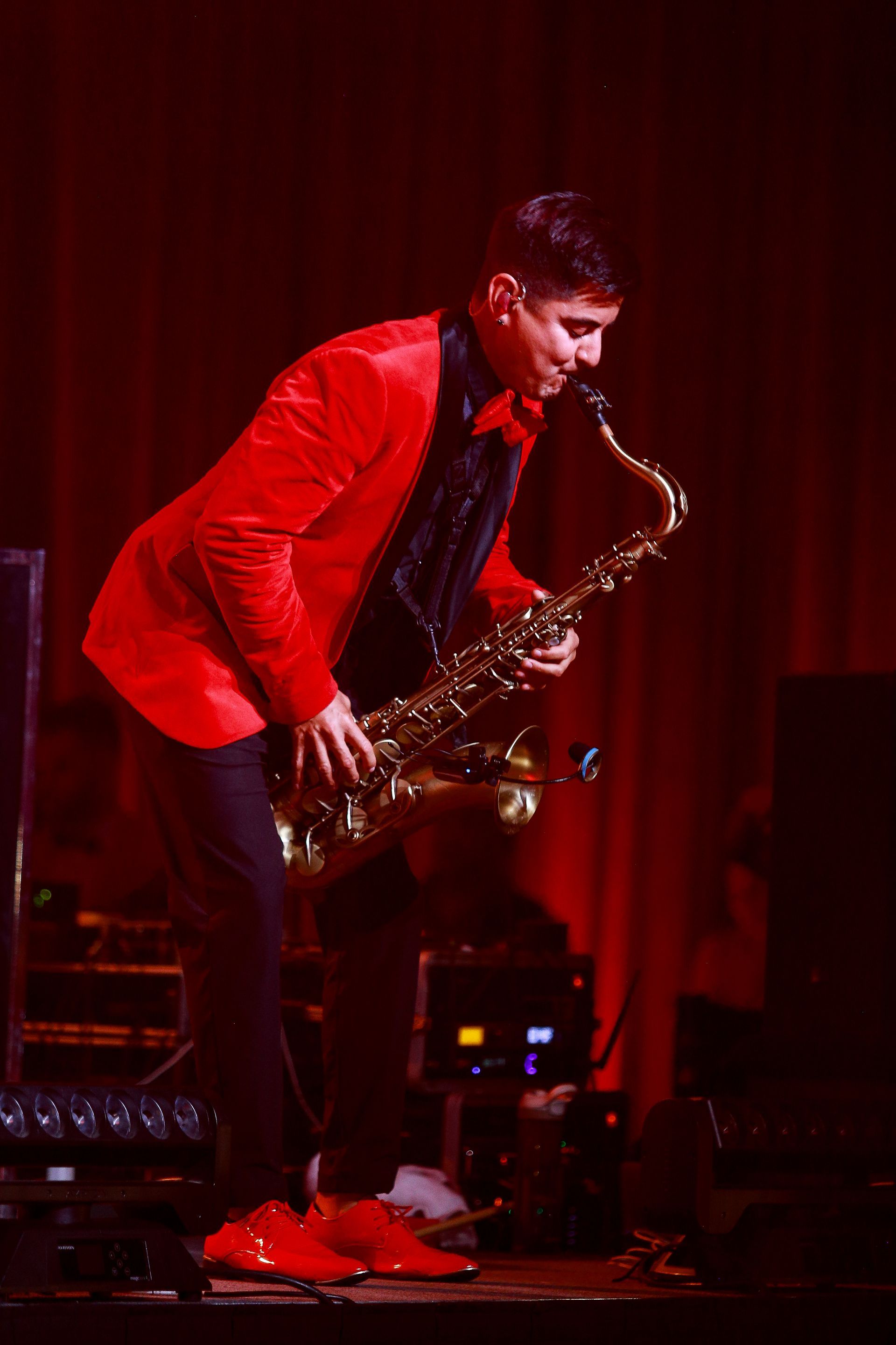 Man in red suit plays saxophone on a stage with red lighting.