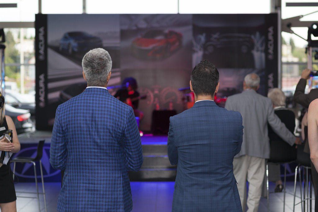 A group of people are standing in front of a stage in a car dealership.