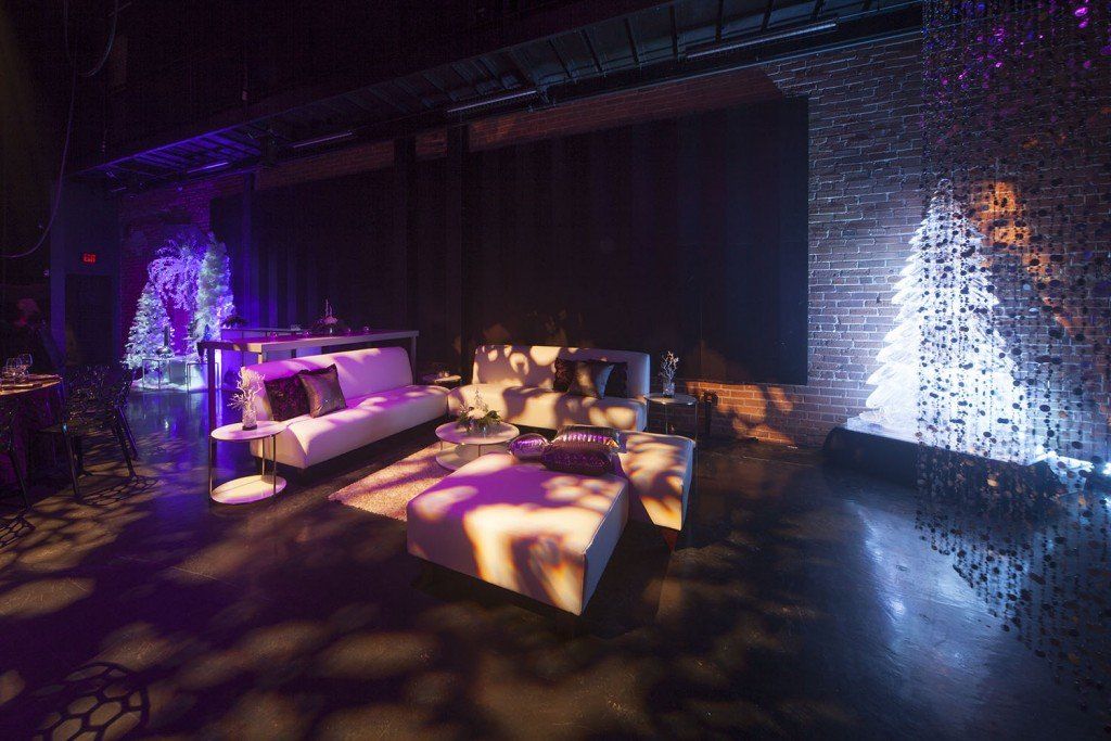 A living room with a couch and a table in a dark room with purple lights.