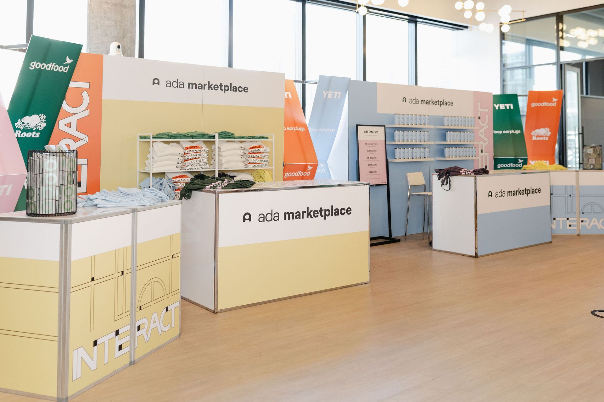 Event booths with pastel colors at a marketplace. Products displayed, people behind counters.