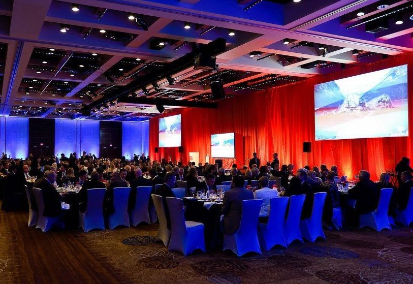 A large room with tables and chairs and a large screen.