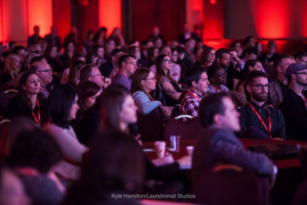 A large group of people are sitting in a room with red lights.