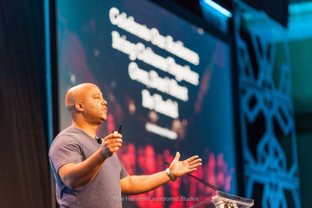 A man is giving a speech in front of a large screen.