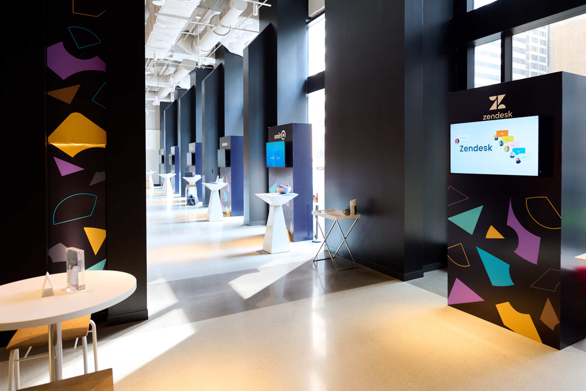 A long hallway with tables and chairs and a large screen on the wall.