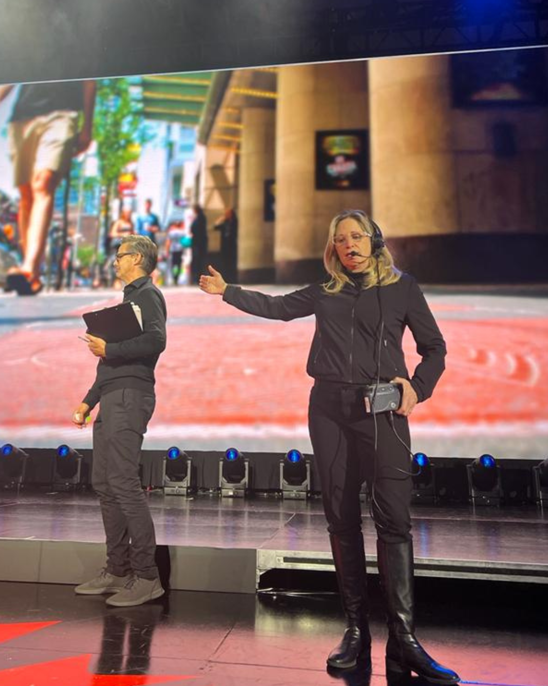 Two women standing on a stage with a large screen behind them