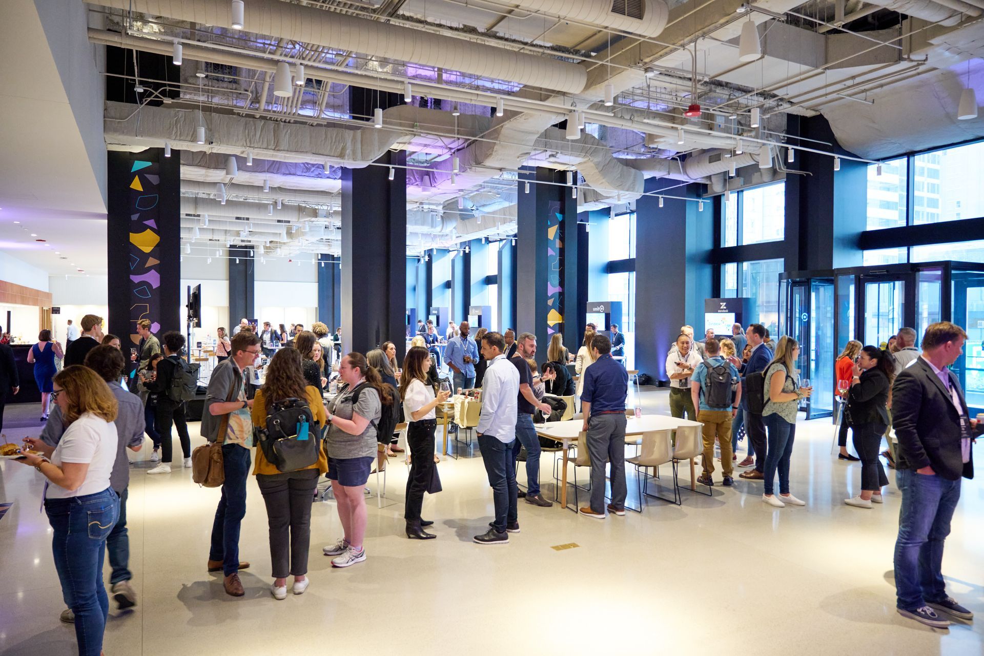 A large group of people are standing in a large room talking to each other.