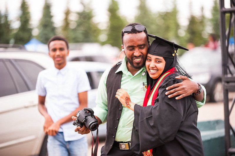 A man is hugging a woman in a graduation cap and gown.