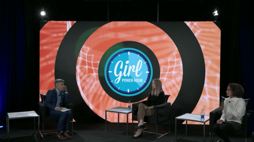 A group of people are sitting in front of a large screen that says girl