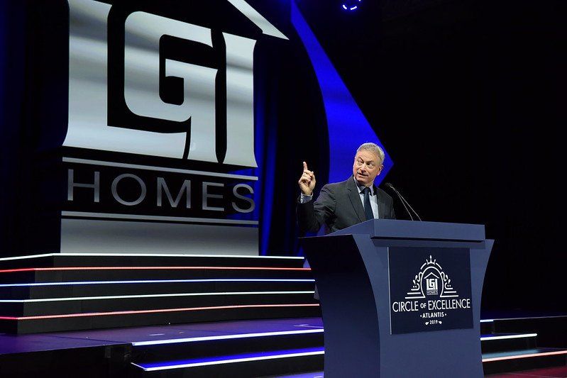 A man stands at a podium in front of a gi homes logo