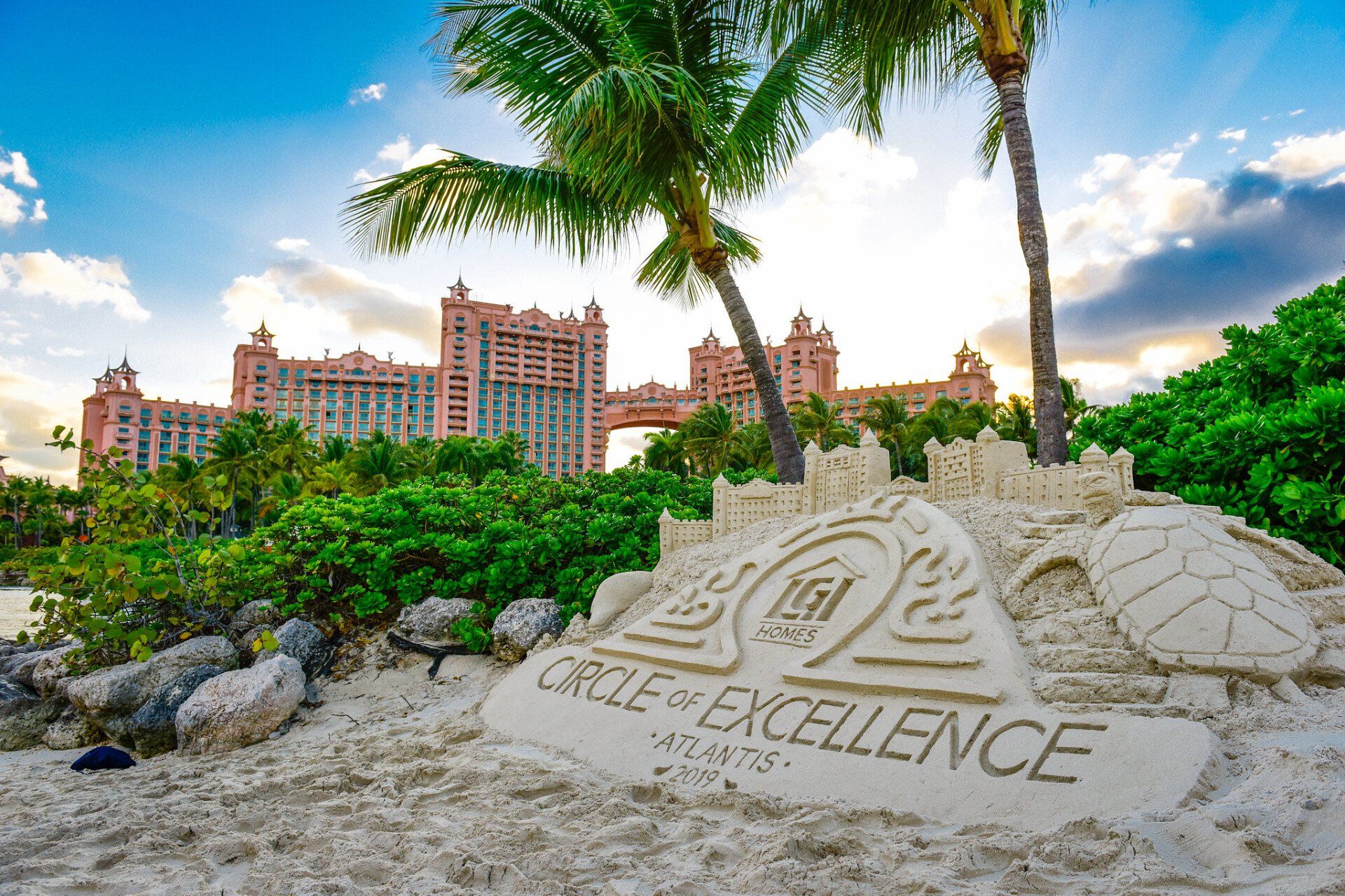 A sand sculpture on a beach with palm trees and a building in the background.
