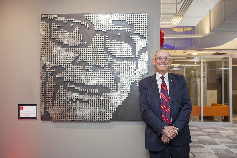 A man in a suit and tie is standing in front of a painting of a man 's face.