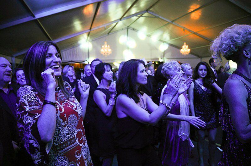 A group of people are dancing in a tent with purple lights.