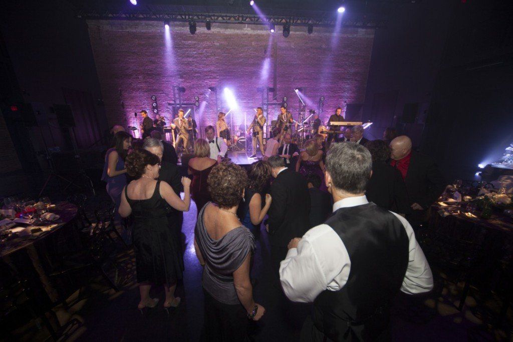 A group of people are dancing in a dark room at a party.