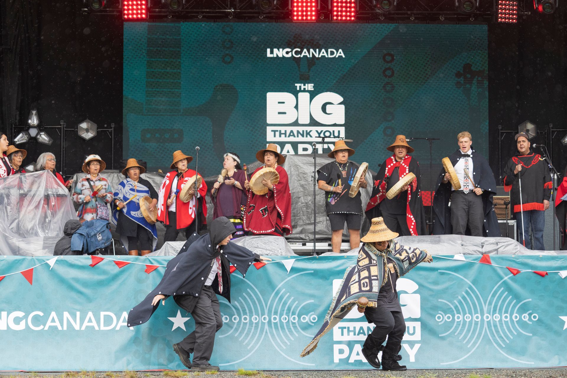 People performing on stage at an event: drummers, dancers, colorful clothing. 