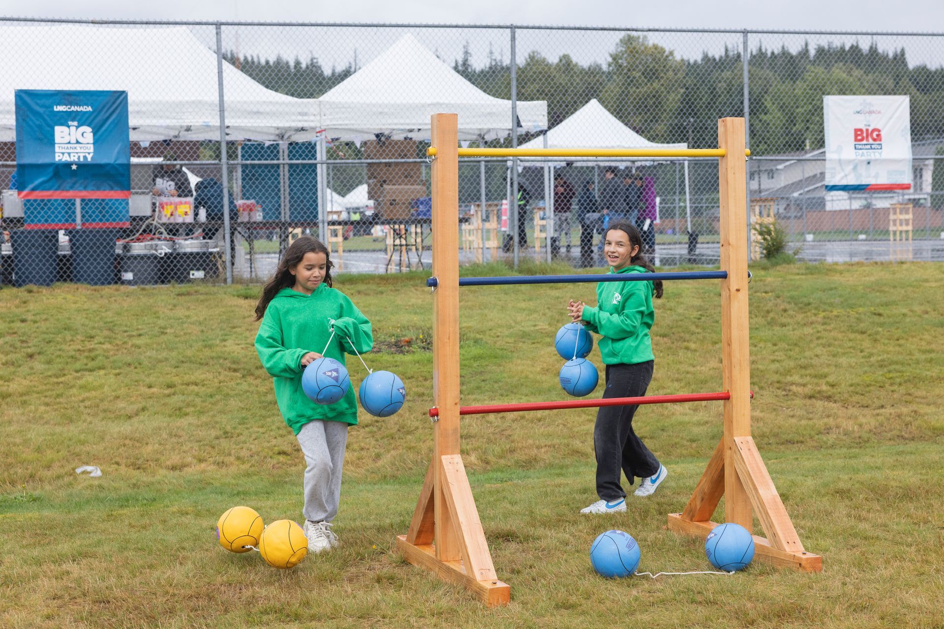 Two girls in green shirts playing ladder toss game on grassy field.