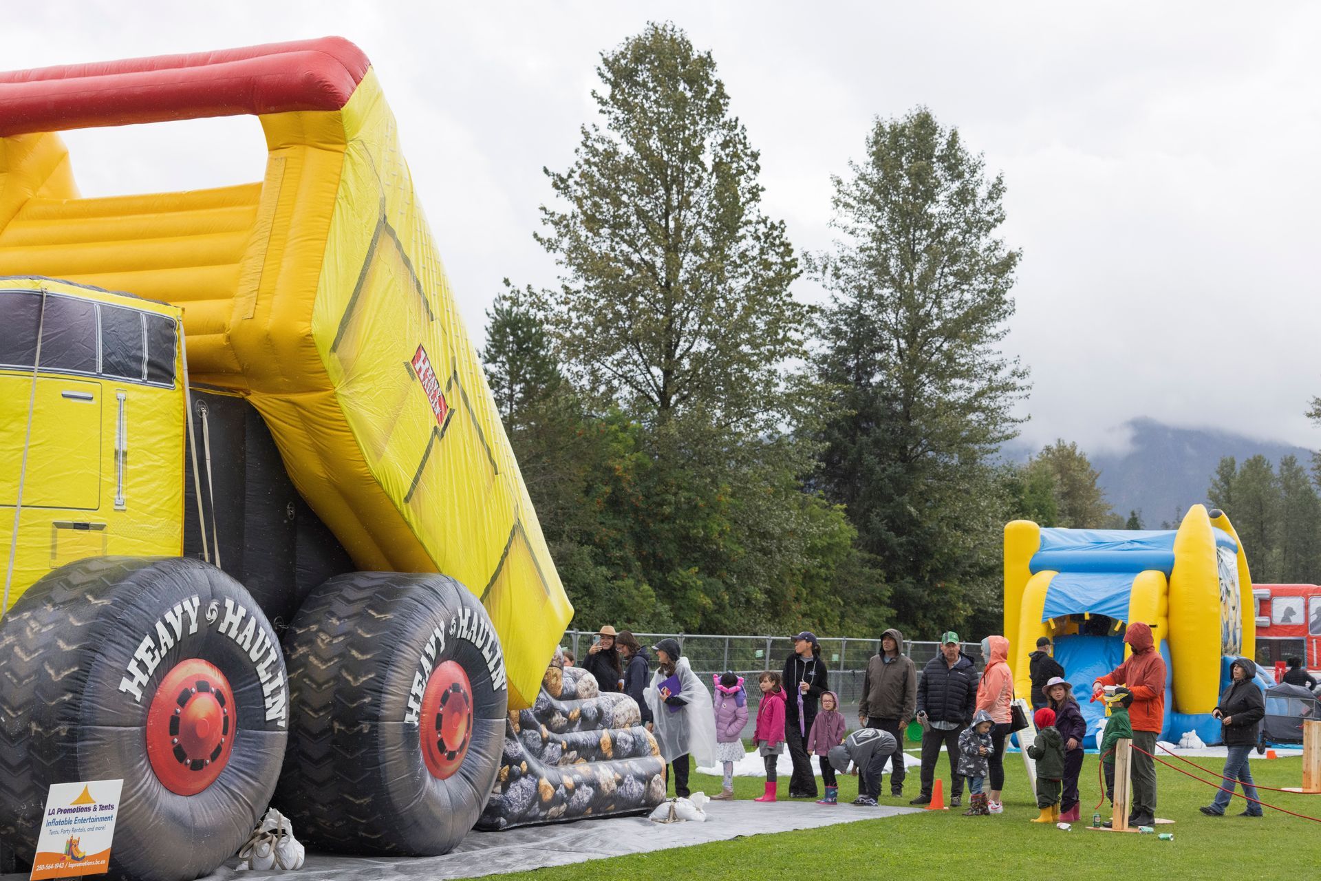 Large inflatable dump truck and bouncy house with people gathered outdoors.