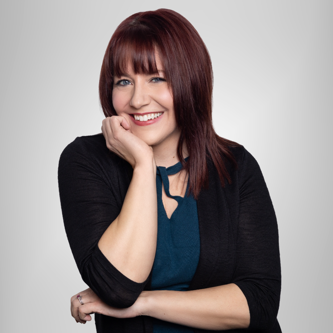 A woman with red hair is smiling with her hand on her chin