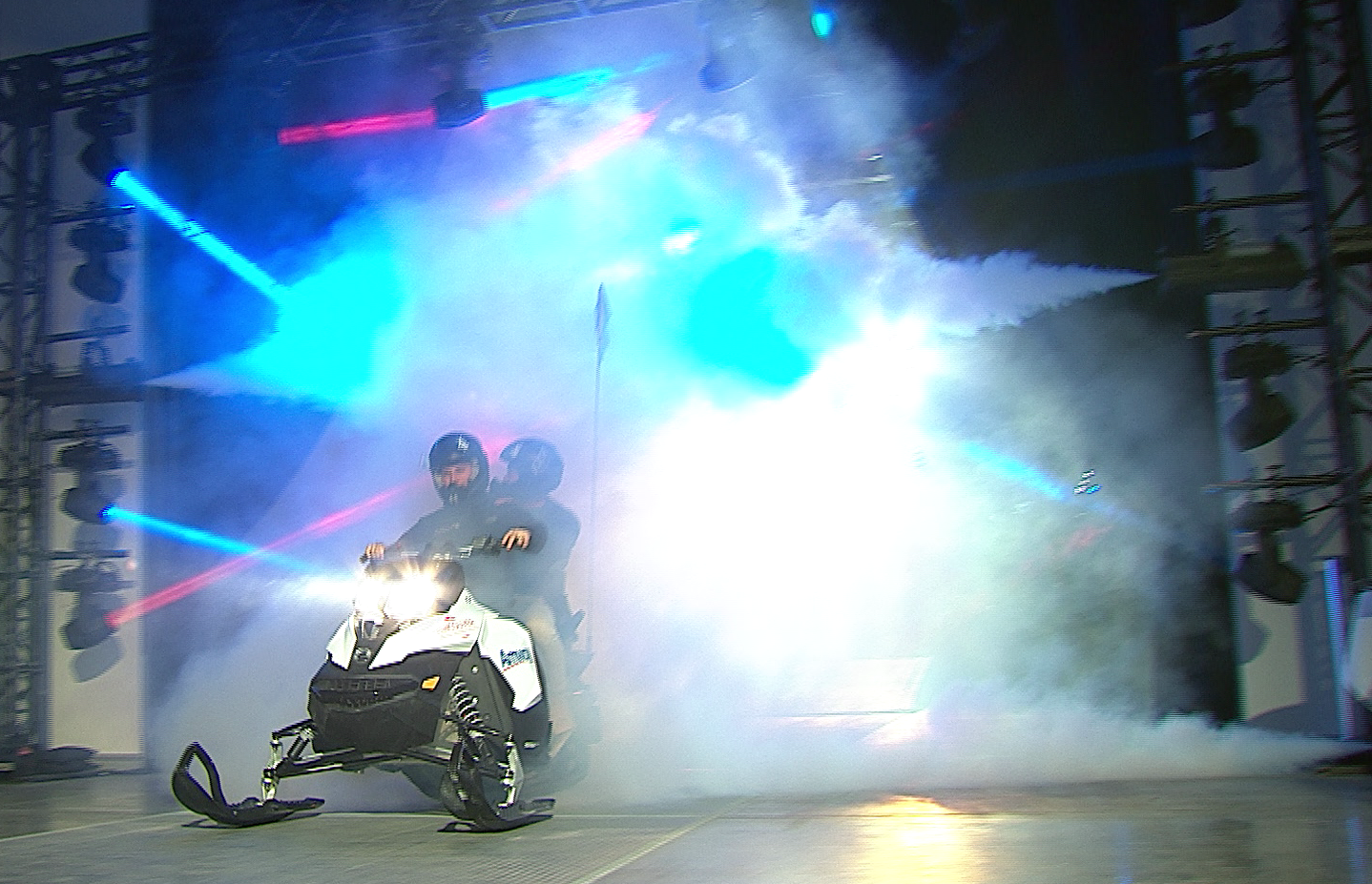 A man is riding a snowmobile on a stage with smoke coming out of it