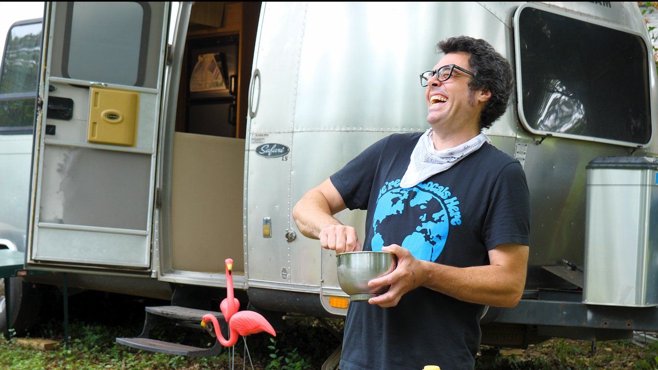A man standing in front of an airstream holding a bowl