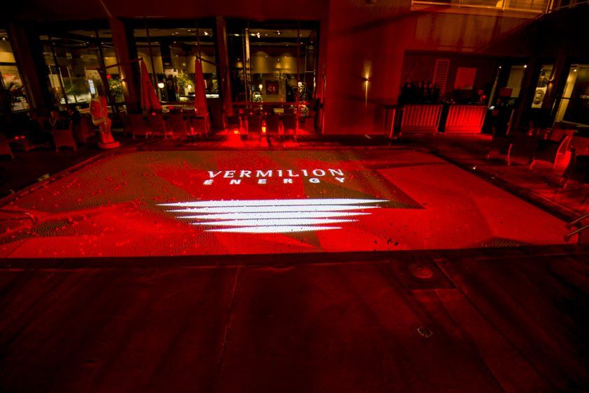 A red and white logo is projected on a dance floor.