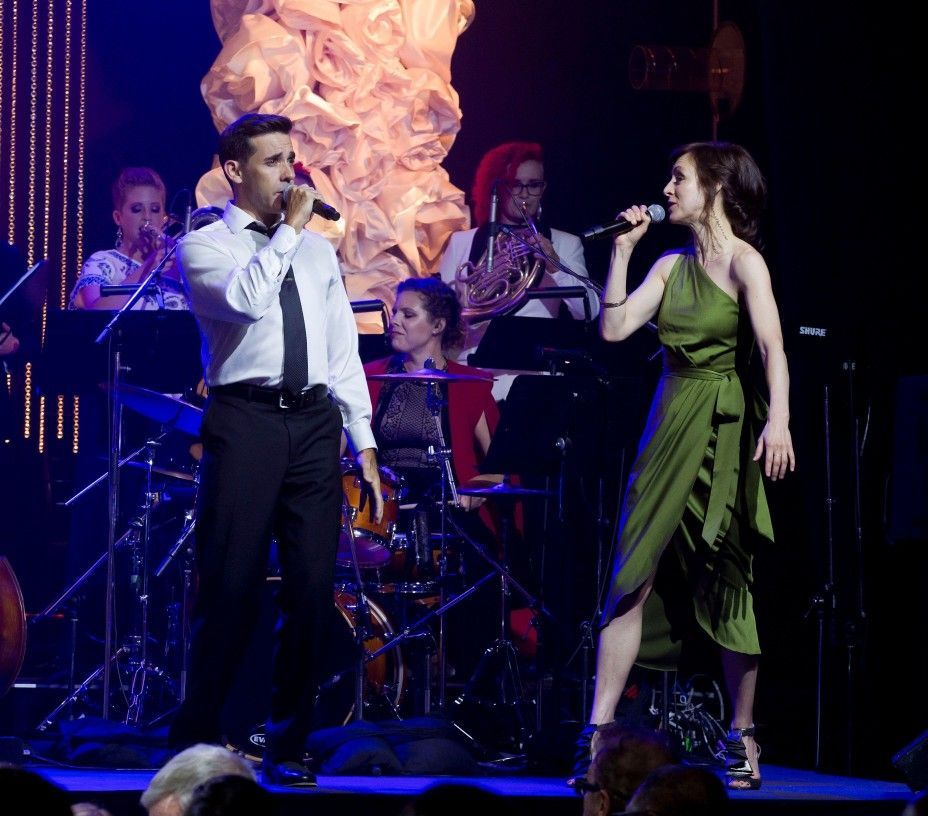 A man singing into a microphone next to a woman in a green dress