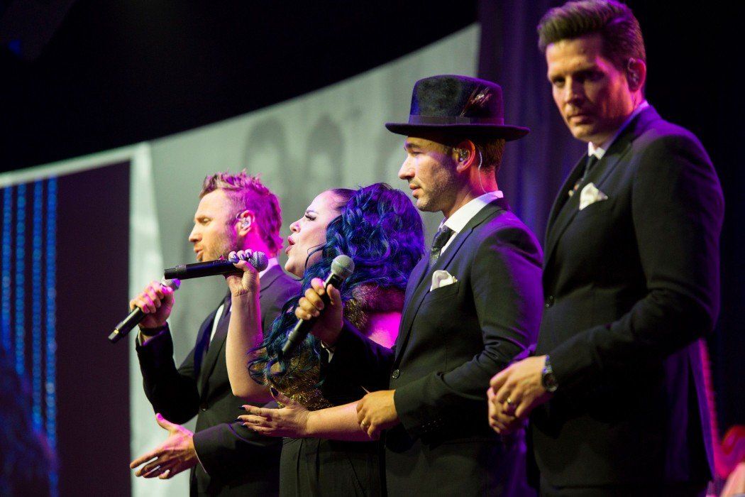 A group of people are singing into microphones on a stage.