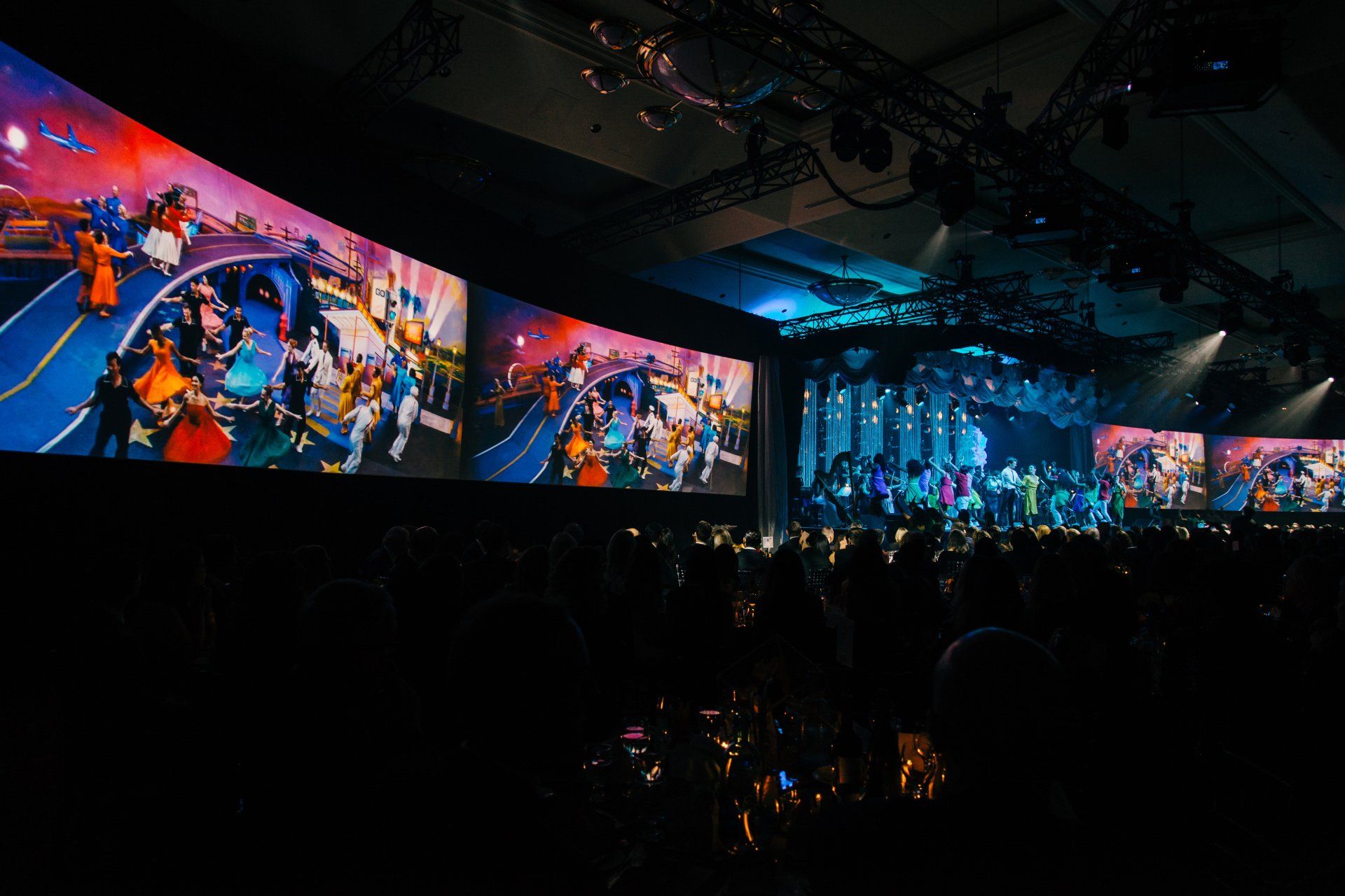 A crowd of people are sitting in front of a large screen at a concert.