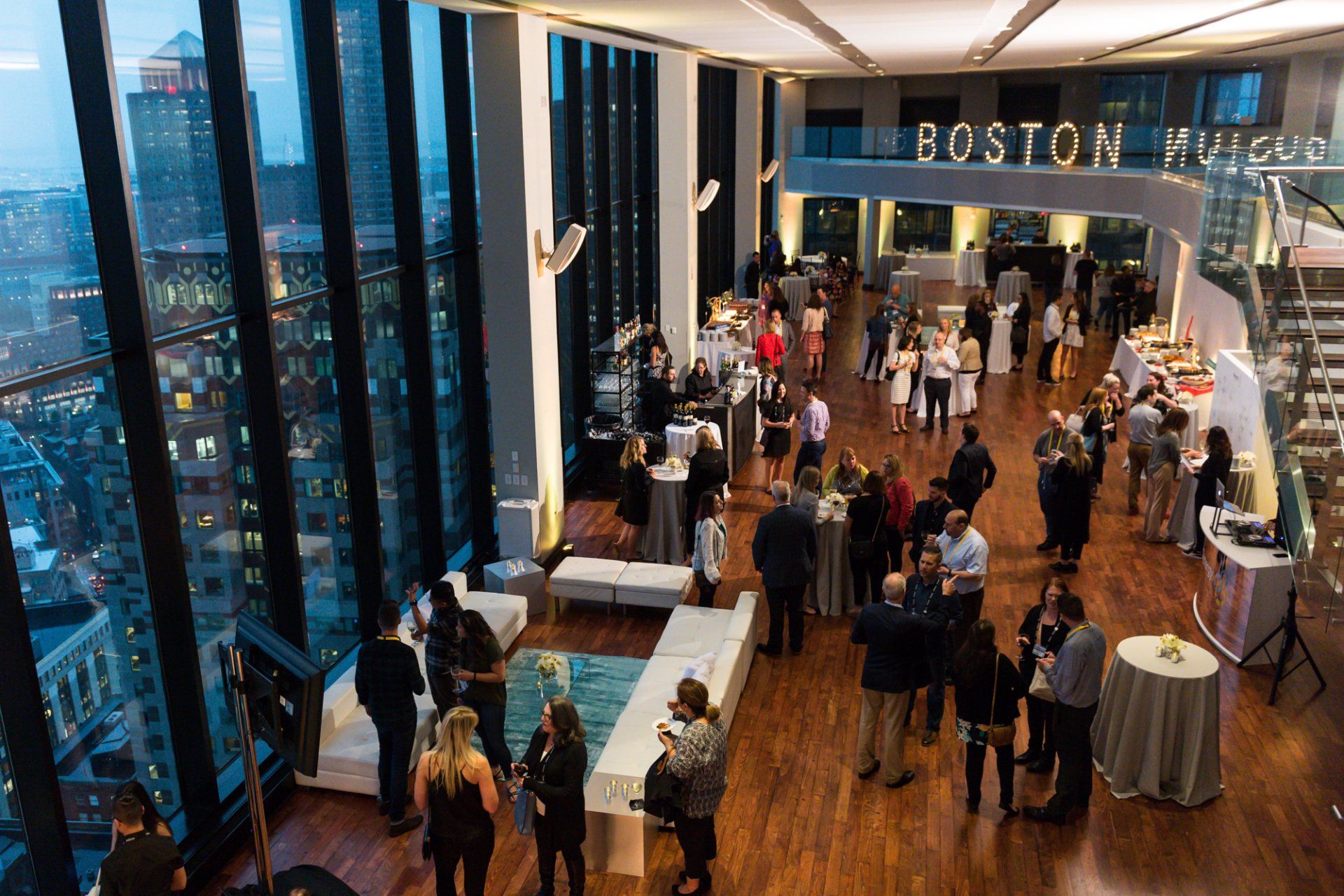 A group of people are standing in a large room with tables and chairs.