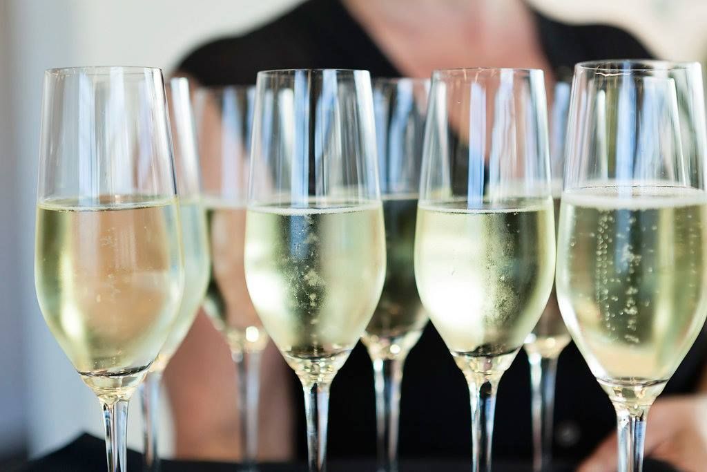 A woman is holding a tray of champagne glasses on a table.
