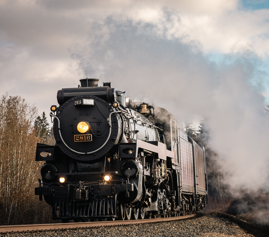 Black steam train on tracks, billowing white smoke, curves through a natural landscape.