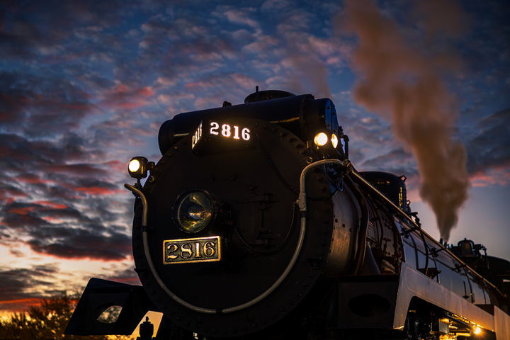 A black train with smoke coming out of it at sunset.