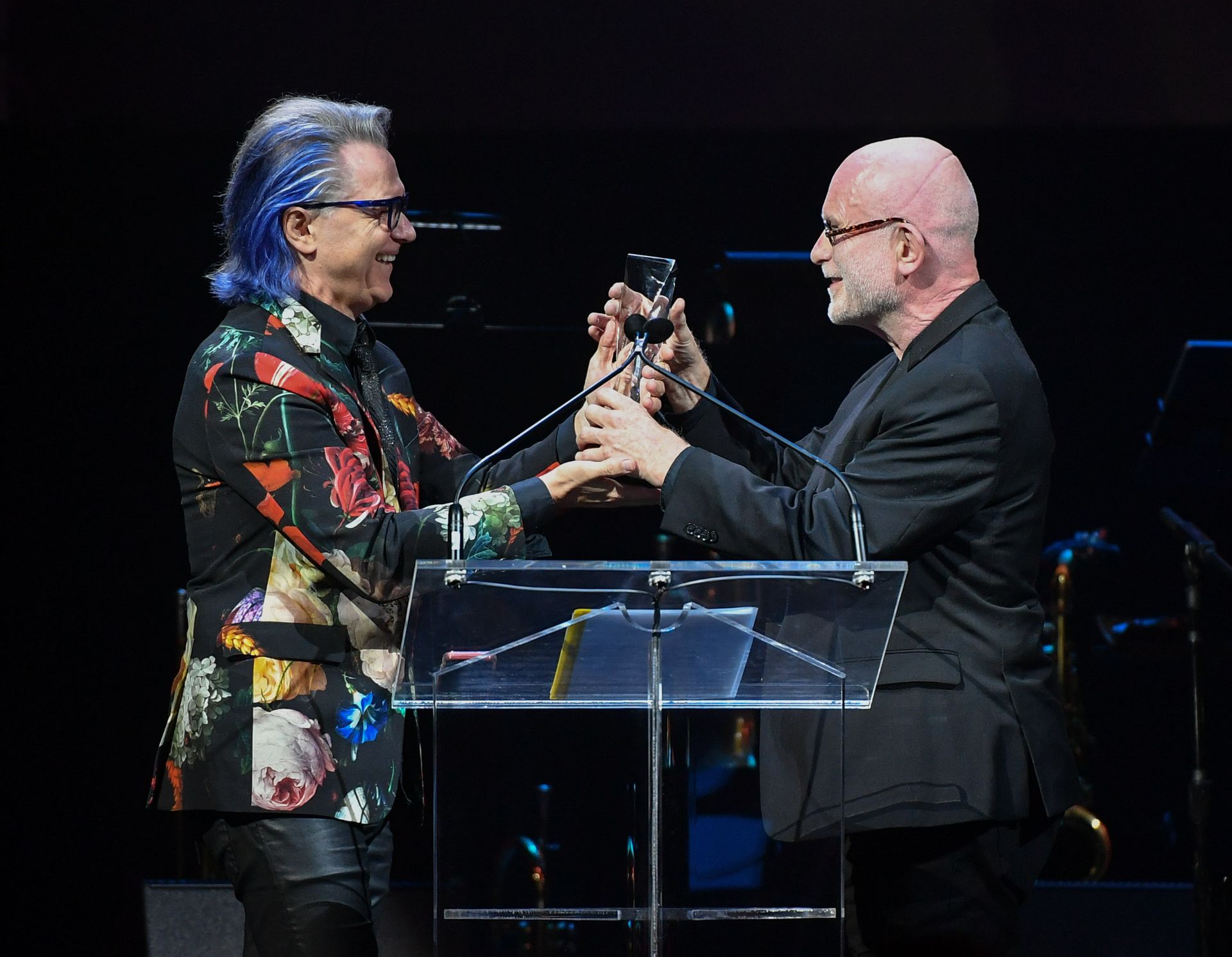 Two men are standing next to each other on a stage and shaking hands.