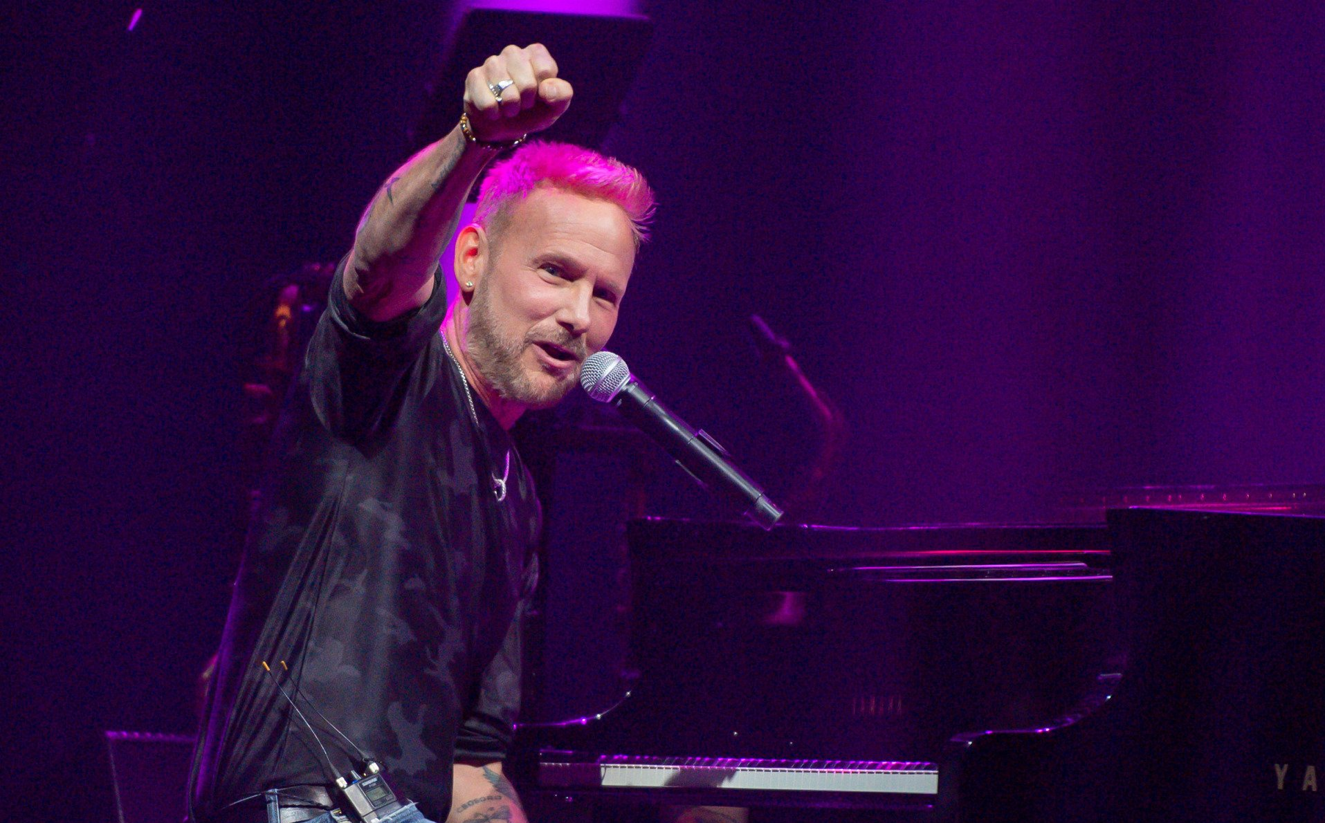 A man is singing into a microphone while playing a piano on a stage.