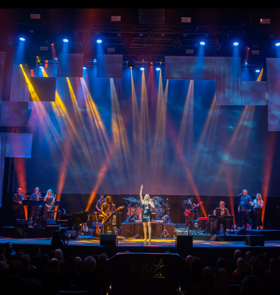 A woman singing on a stage with a band behind her