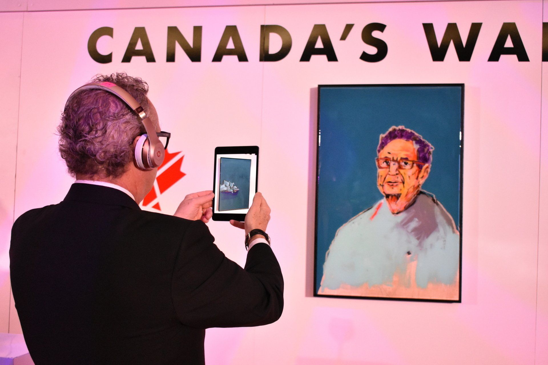 A man is taking a picture of a painting of a man in front of a sign that says canada 's wall