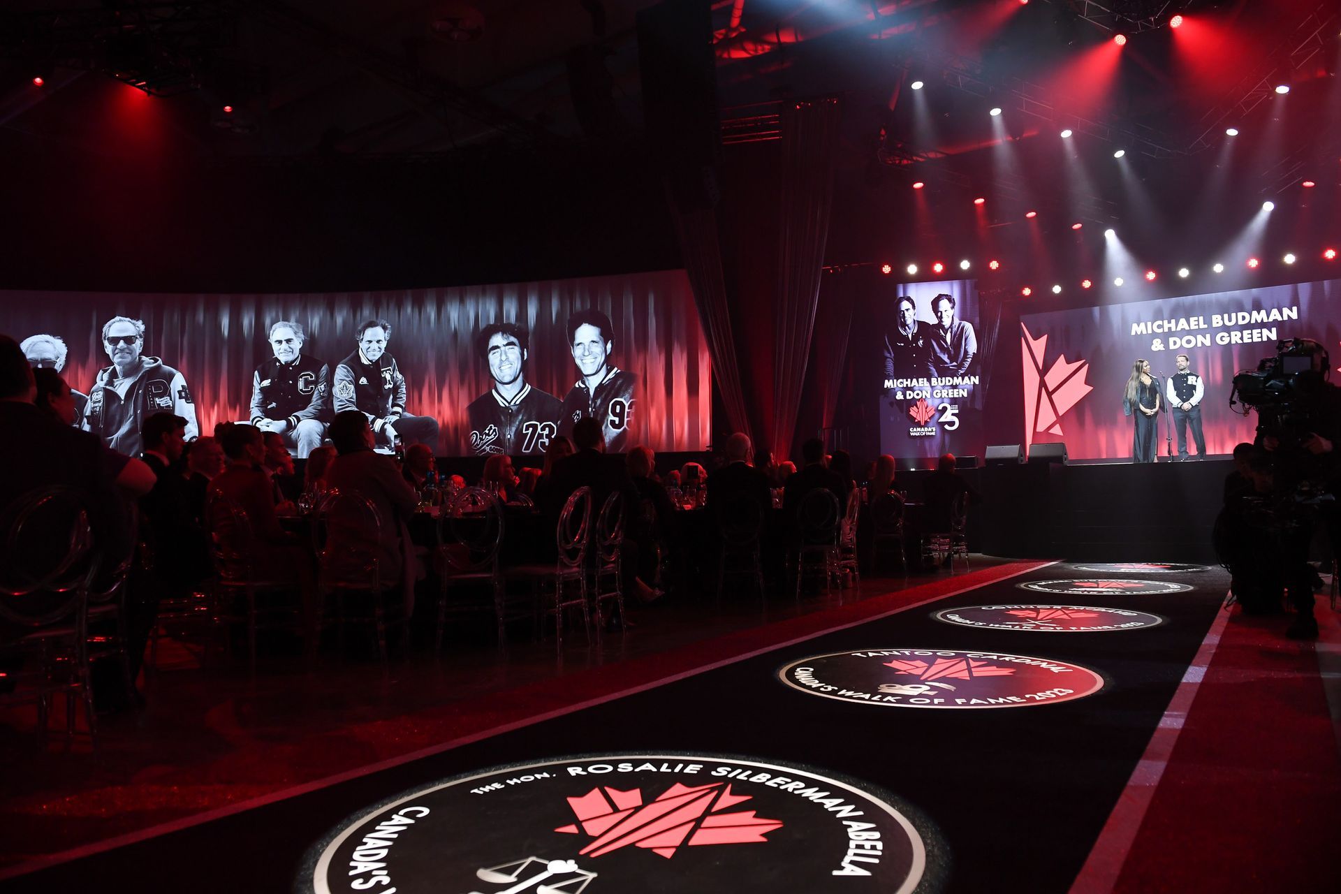 A group of people are sitting at tables in a dark room in front of a stage.