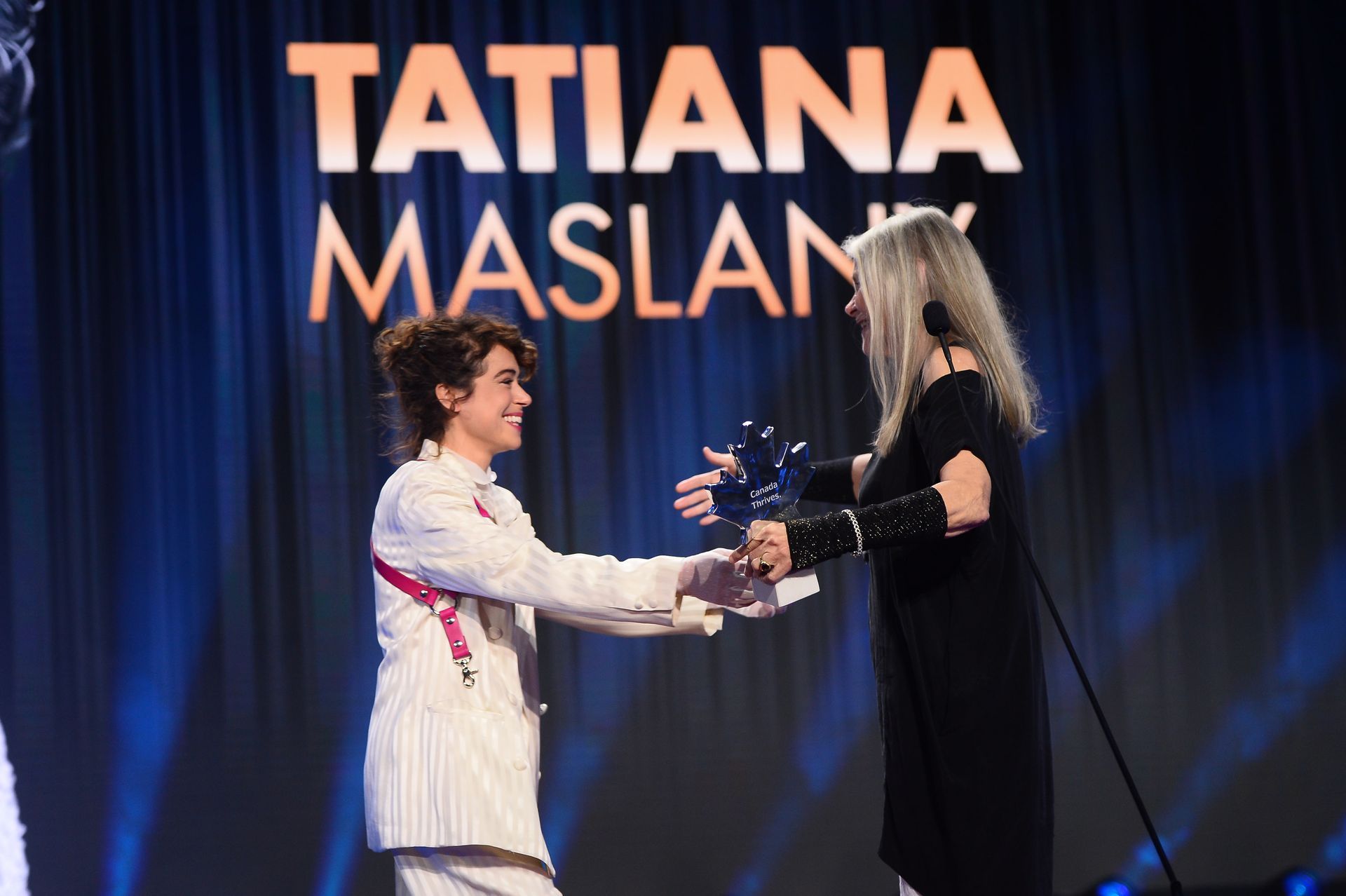 Two women are shaking hands on a stage in front of a curtain.
