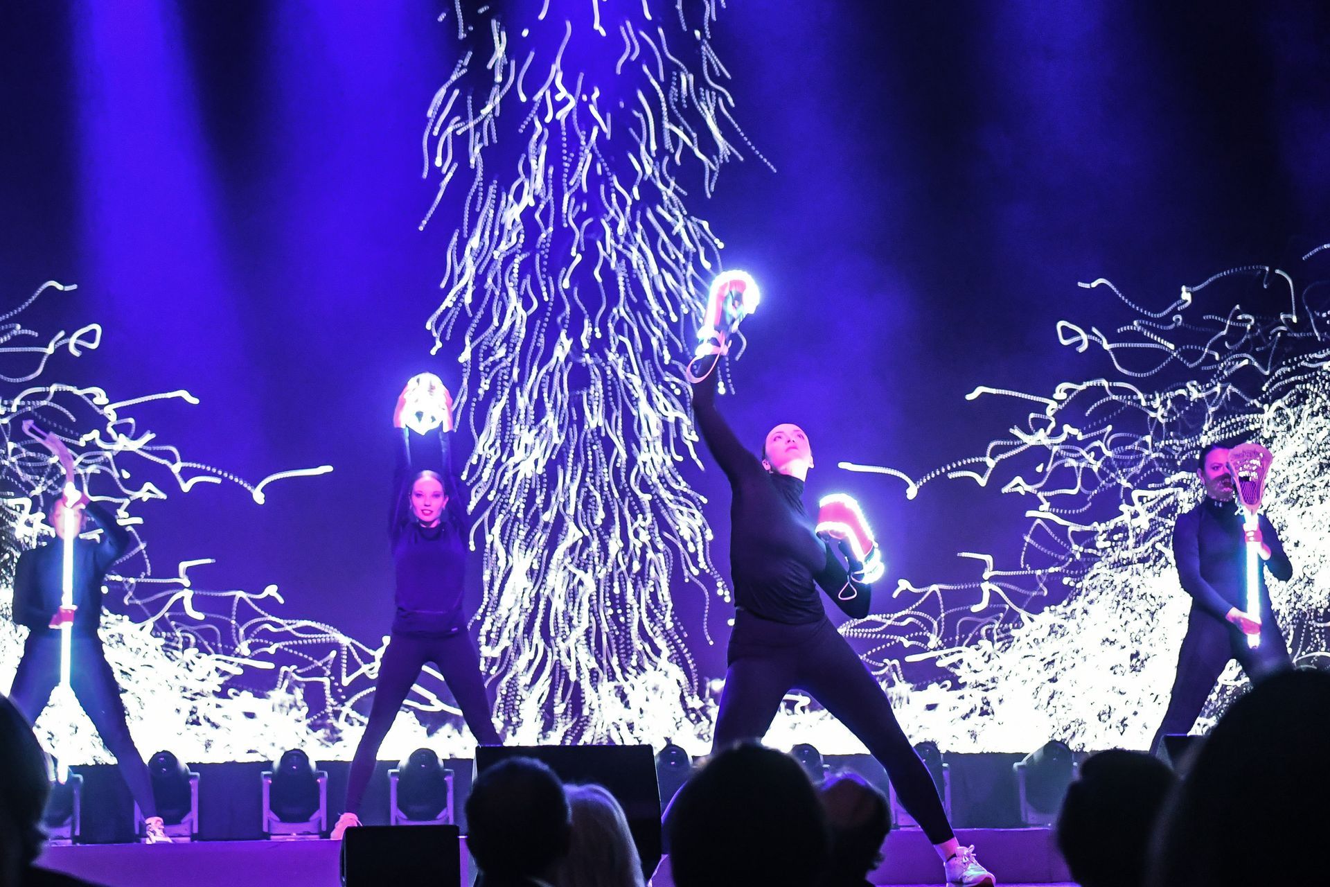 A group of people are dancing on a stage with purple lights behind them