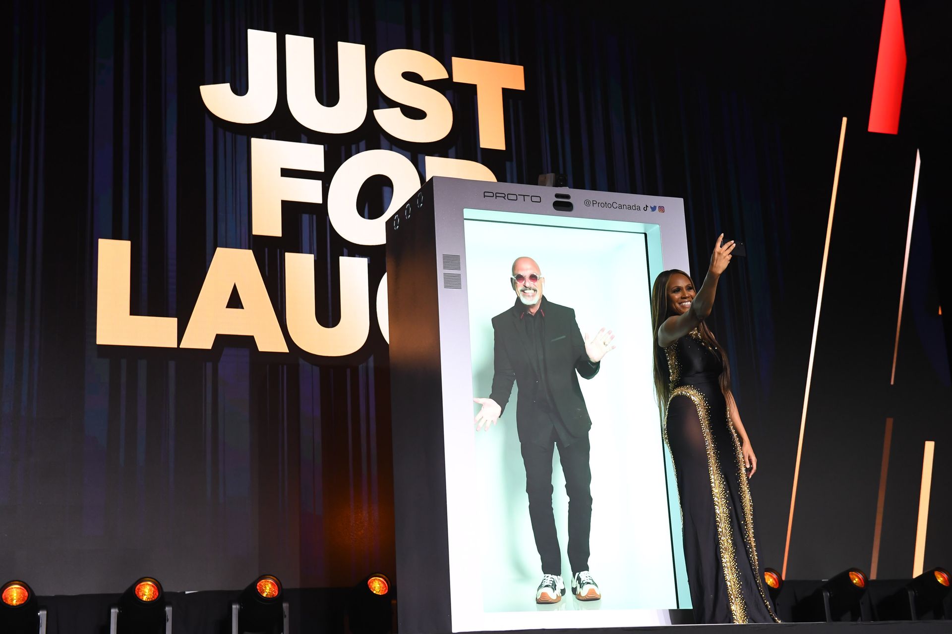 A woman is standing in front of a screen that says just for laugh
