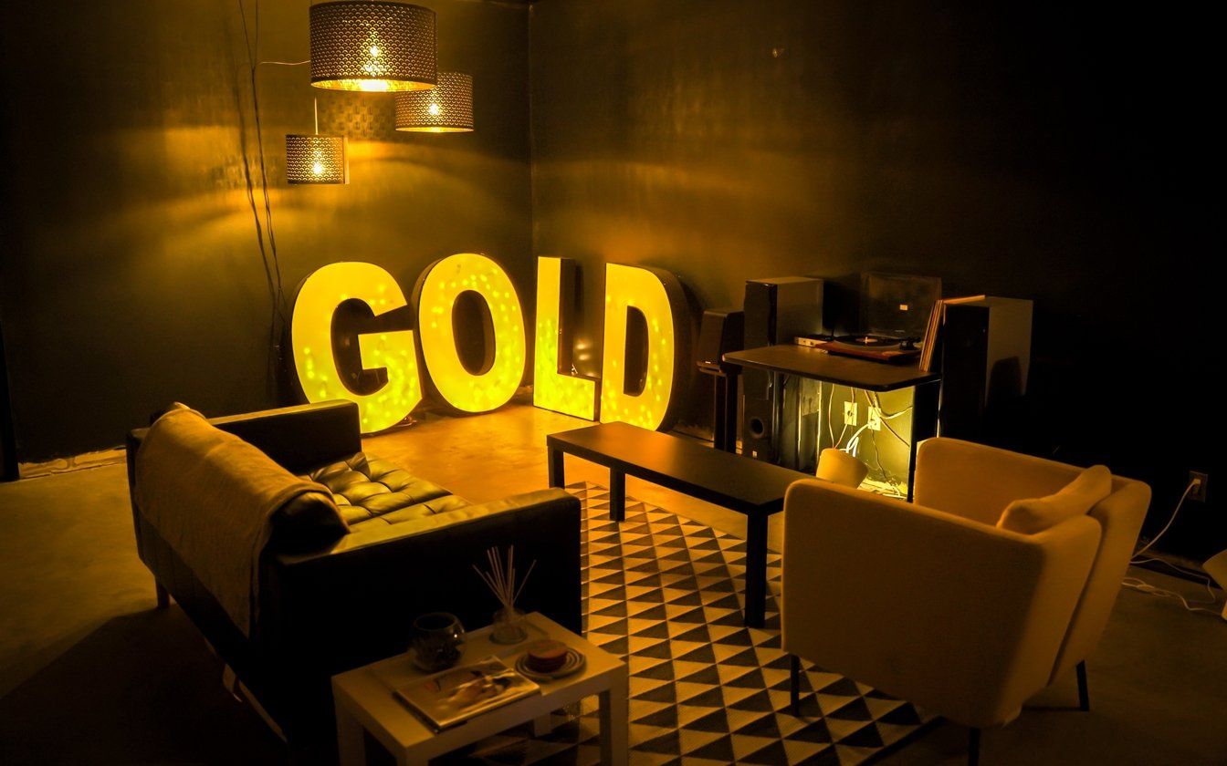 A living room with a couch and chairs and a gold sign on the wall.