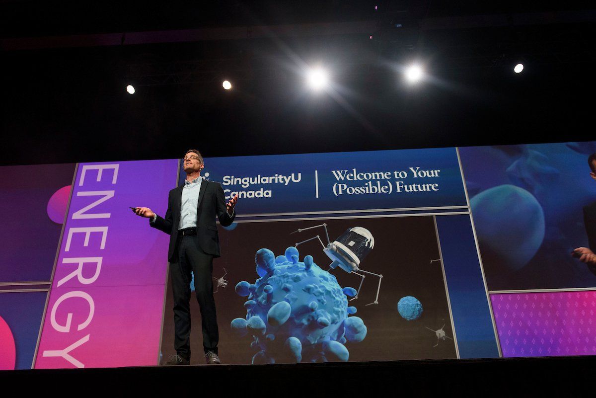 A man stands on a stage in front of a large screen that says energy