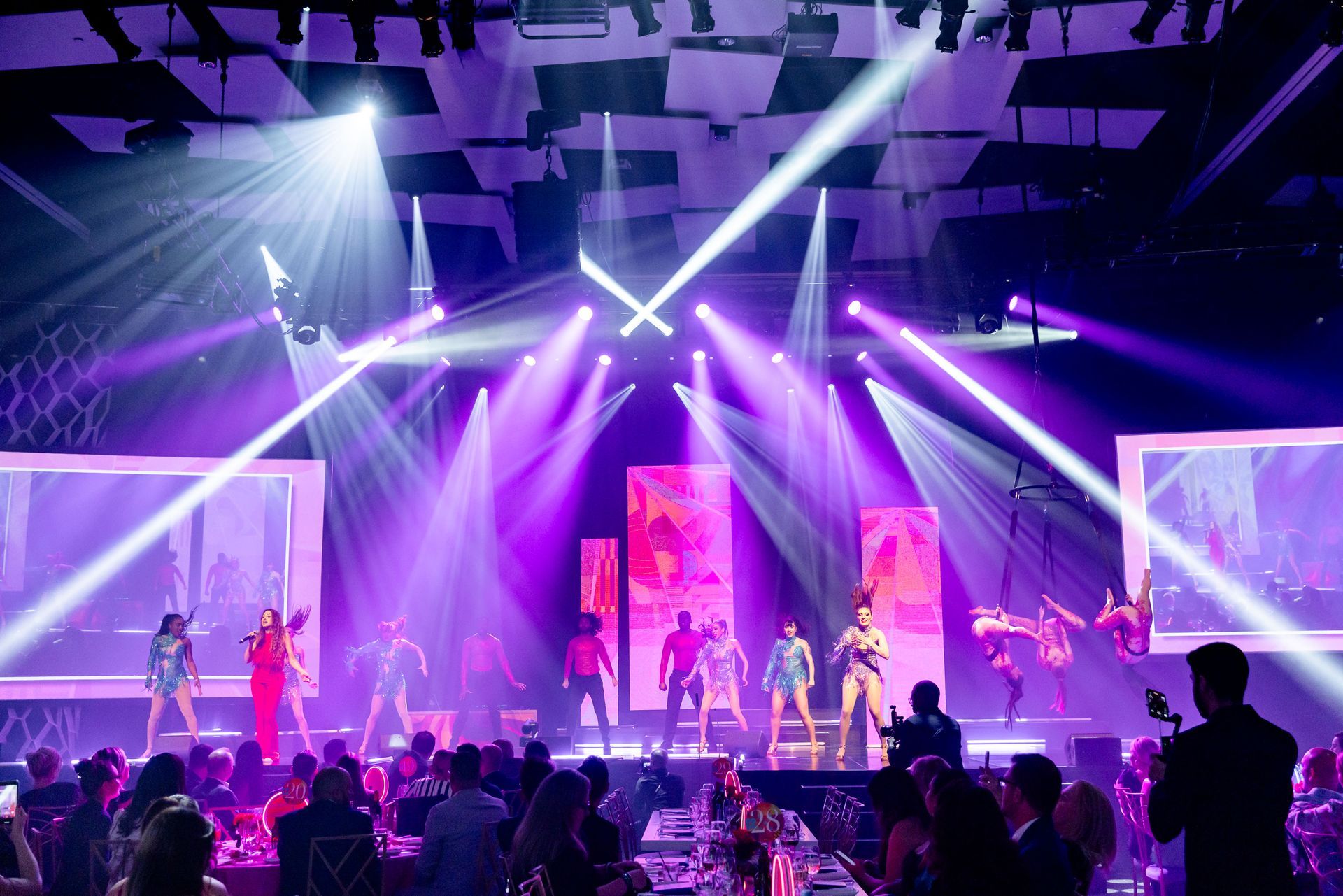 Stage with performers and audience lit with purple and white lights.