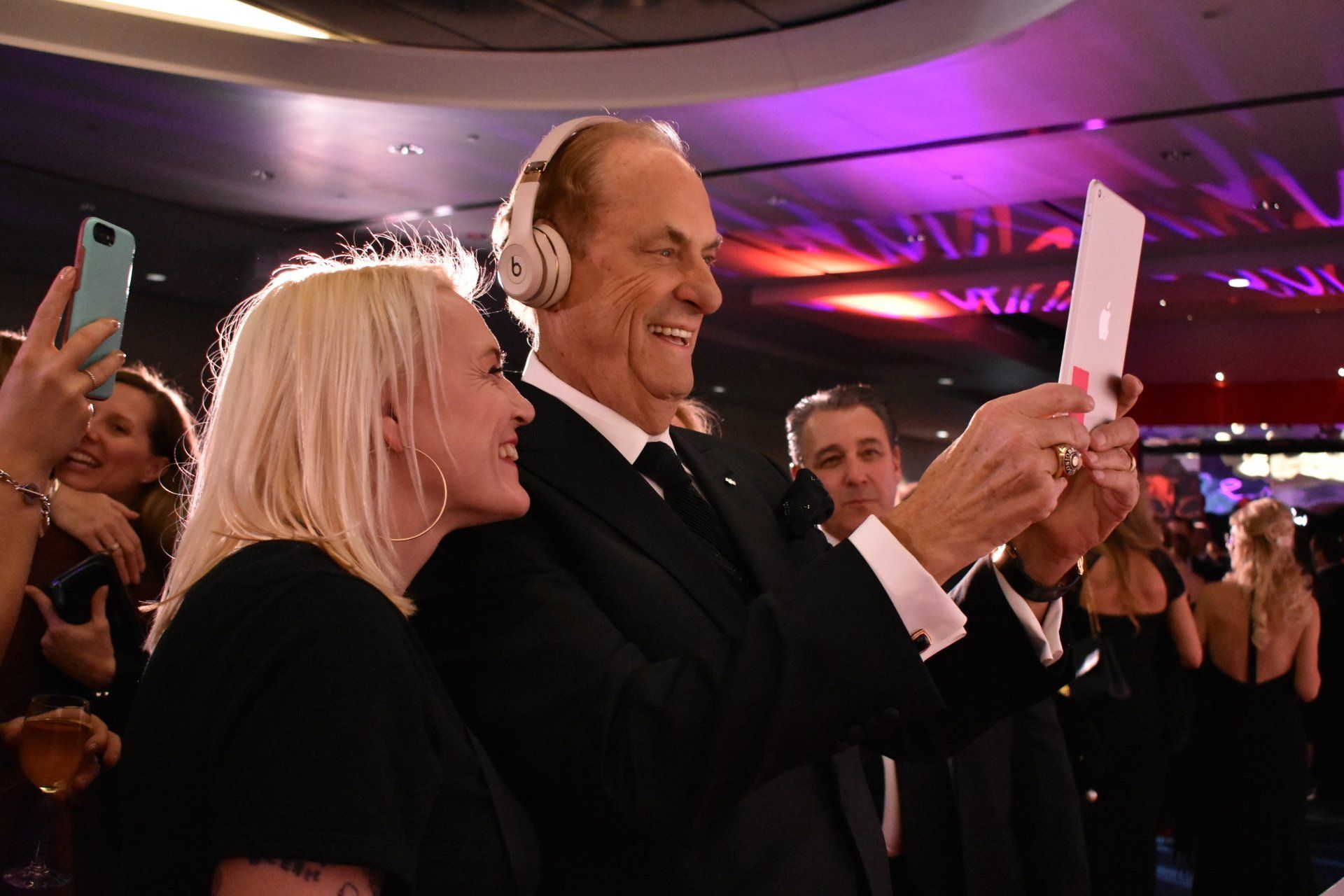 A man wearing headphones is taking a selfie with a woman.
