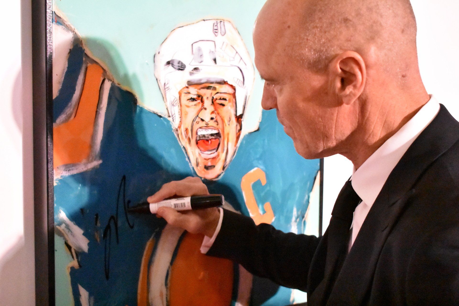 A man in a suit is signing a painting of a hockey player