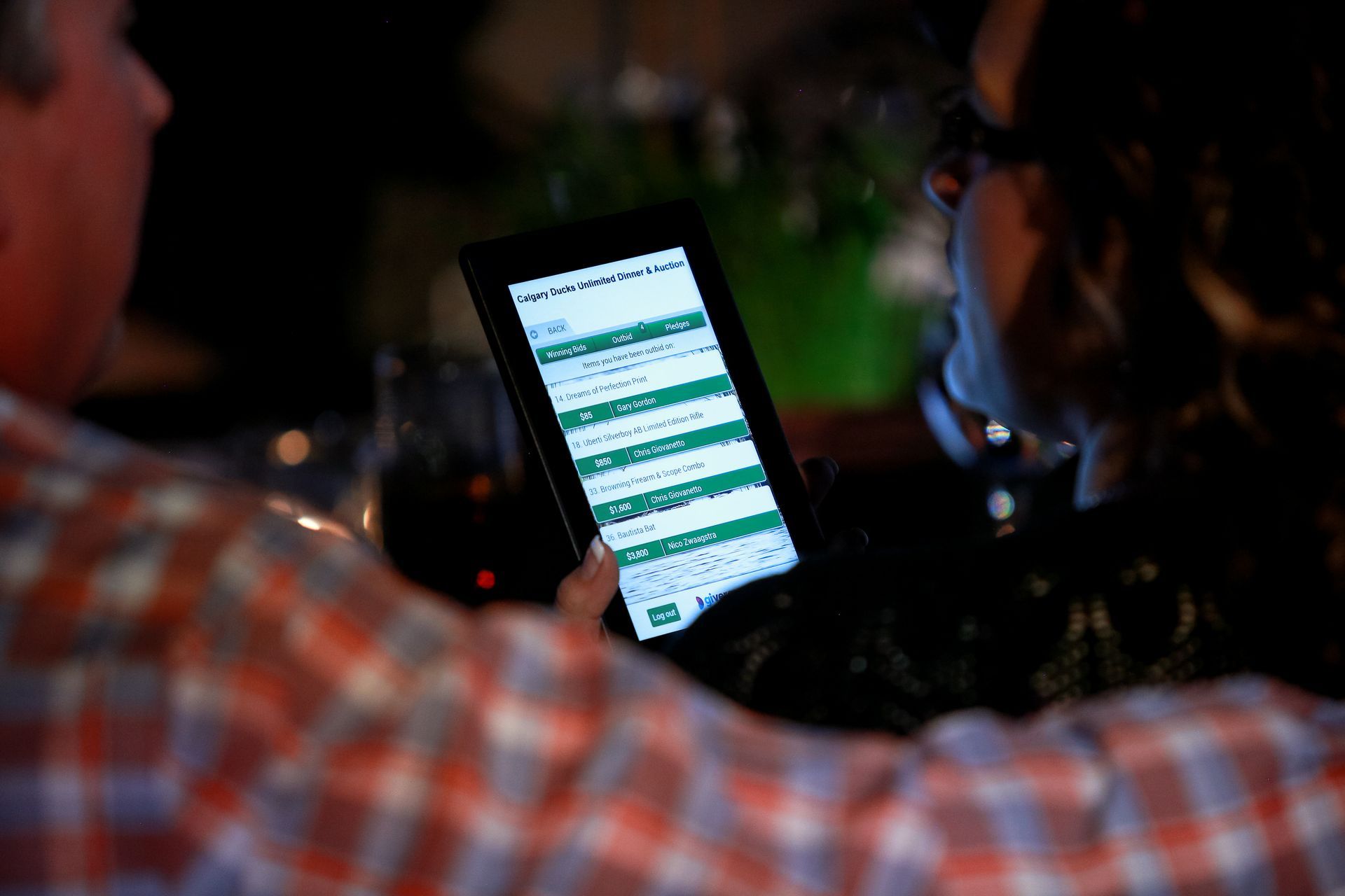 A man is looking at a tablet while another man looks on.