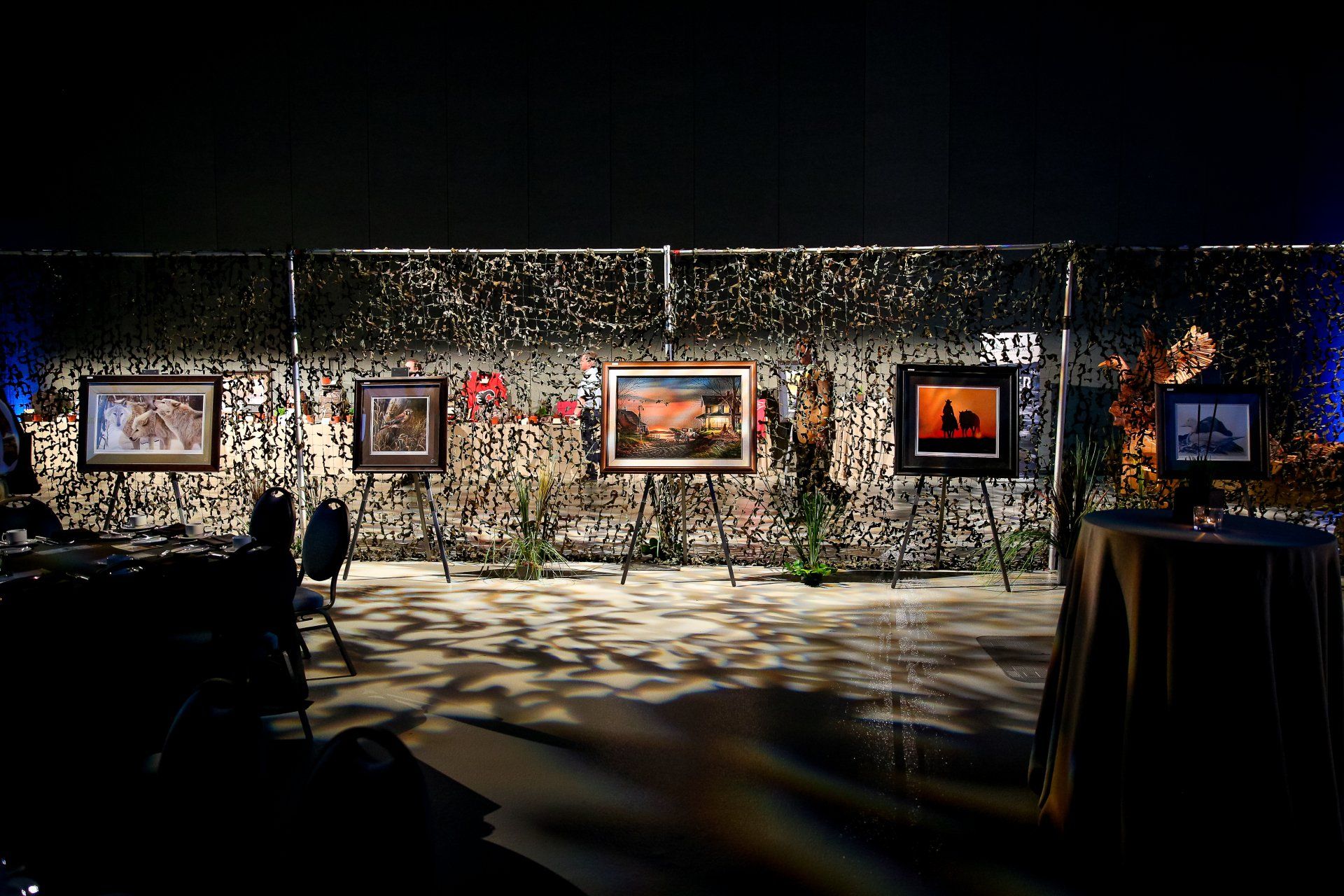 A row of paintings are hanging on a wall in a dark room.