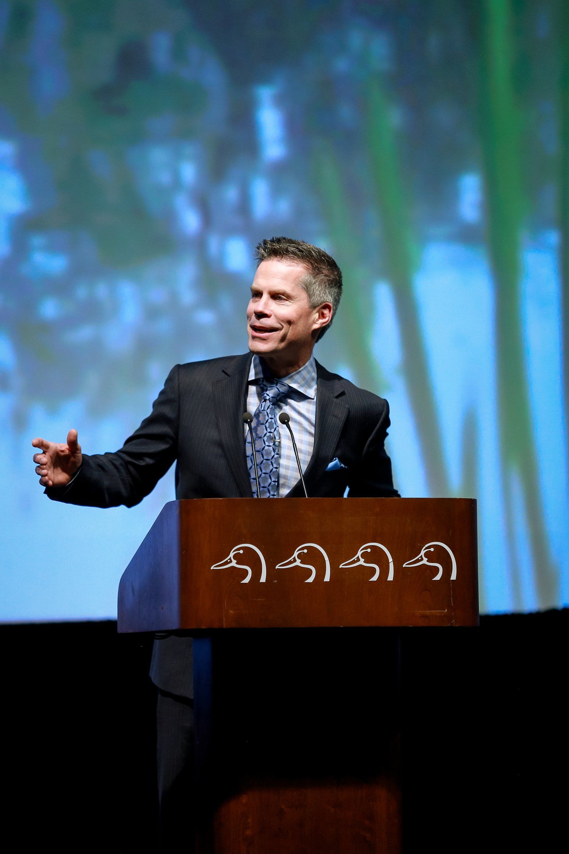 A man in a suit and tie is standing at a podium with a sign that says ' aa ' on it